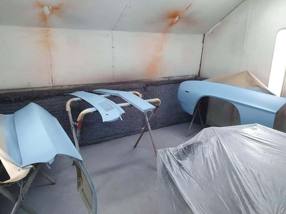 Light blue panels and a quarter panel on trestles inside the spray booth