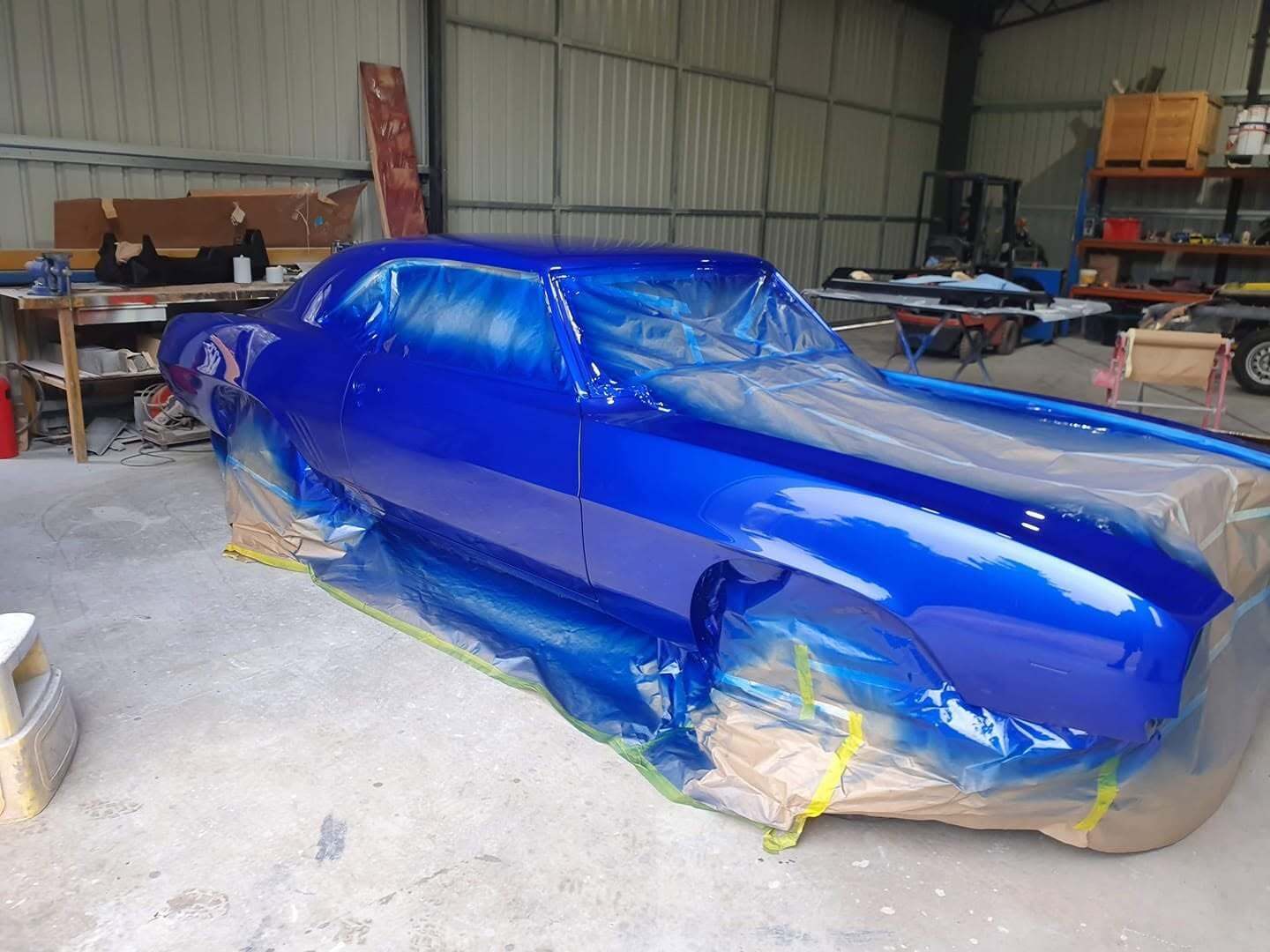 The same Camaro masked in paper and tape in the workshop with fresh blue laid down