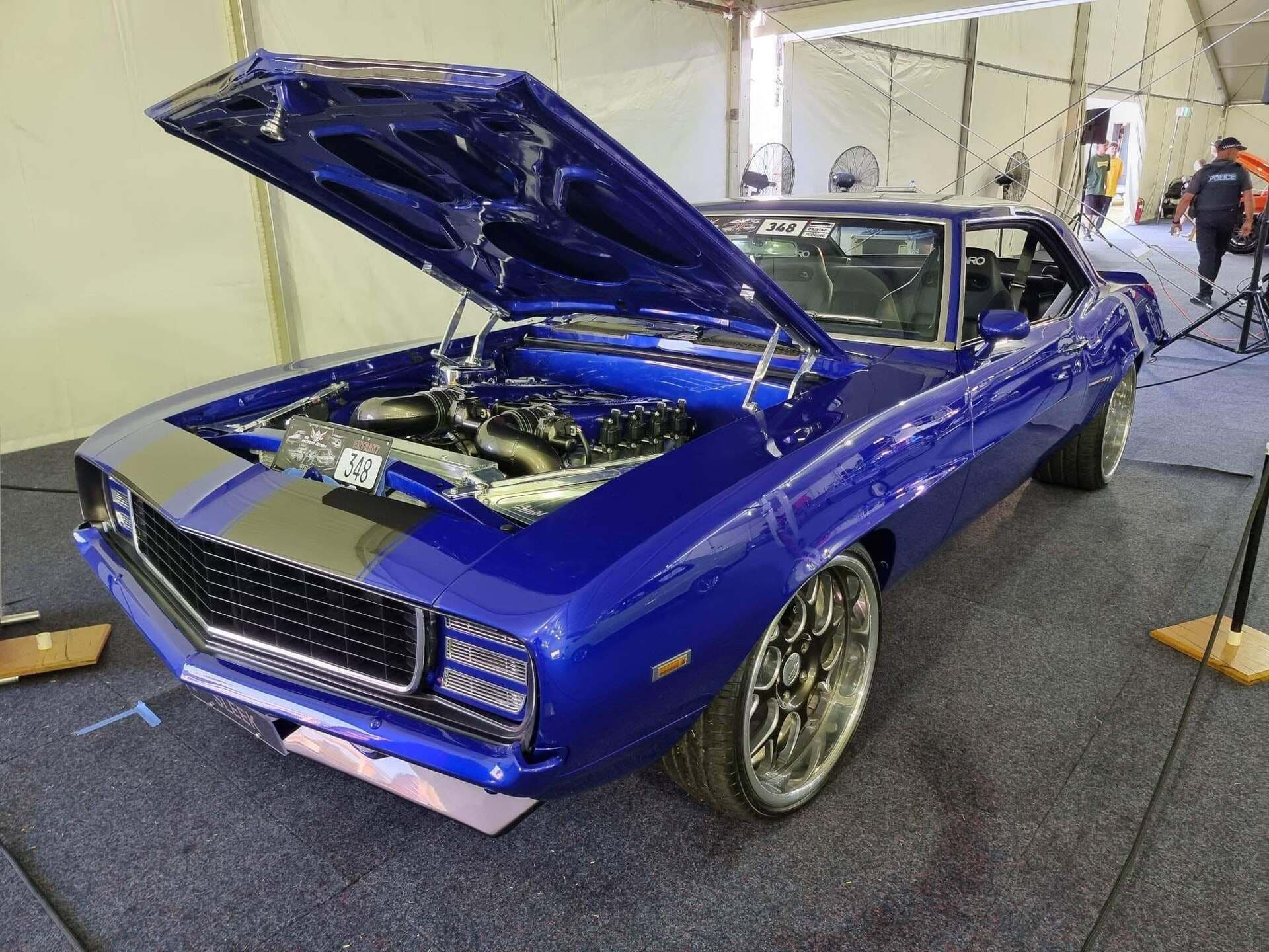 A 1969 Camaro finished in deep blue with silver stripes, bonnet up, on a show stand