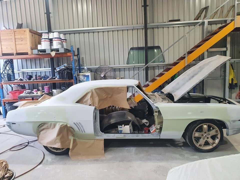 The Camaro stripped to a bare shell in primer, doors off, in the workshop