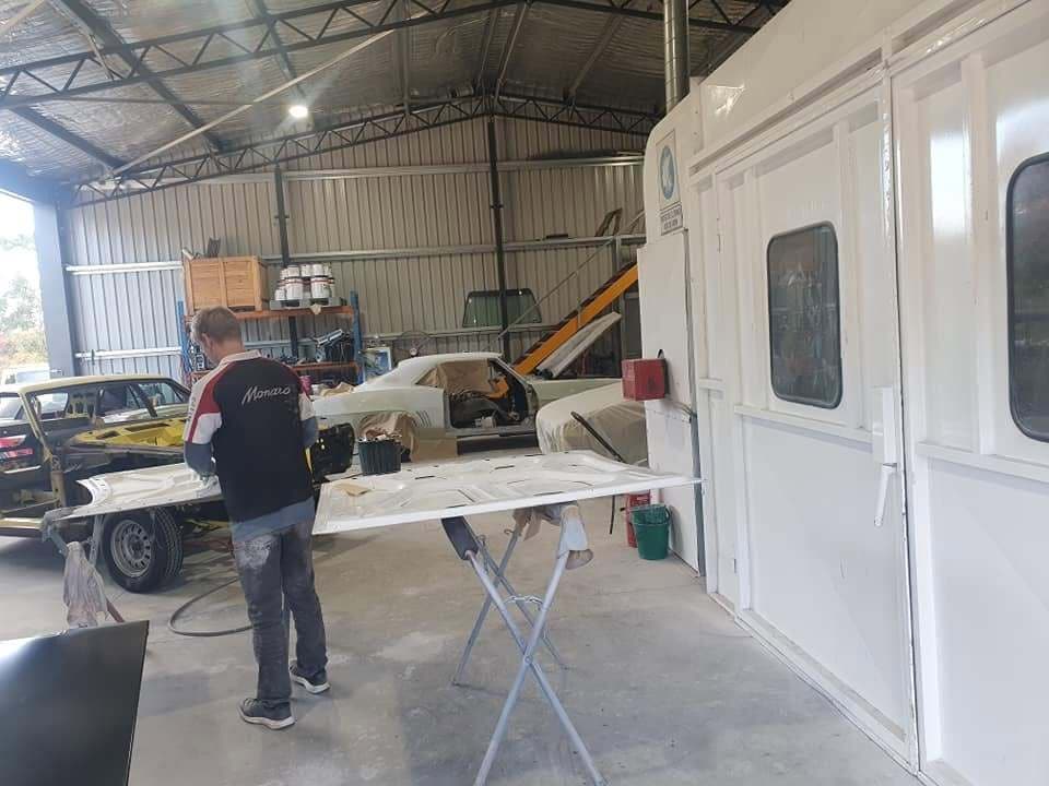 A painter working a panel on trestles beside the spray booth in the workshop